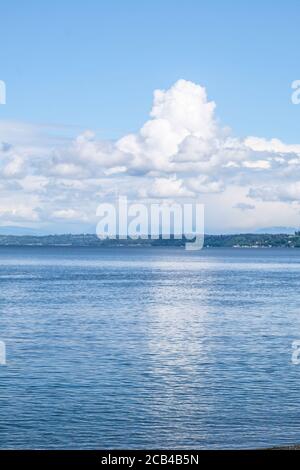 Cumulus nuvole su Isola in Puget suono con riflessione in Acqua di mare Foto Stock