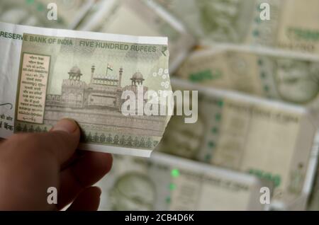 Una mano di donna che tiene una lacerata nuova RS 500 Rupees Banconote in valuta indiana che mostrano il Forte Rosso contro uno sfondo bokeh con un sacco di 500 note Foto Stock