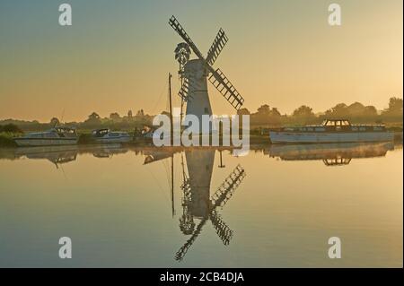 Thurne Dyke drenaggio mulino a vento Norfolk, riflesso nel fiume Thurne all'alba con barche ormeggiate verso la riva del fiume. Foto Stock