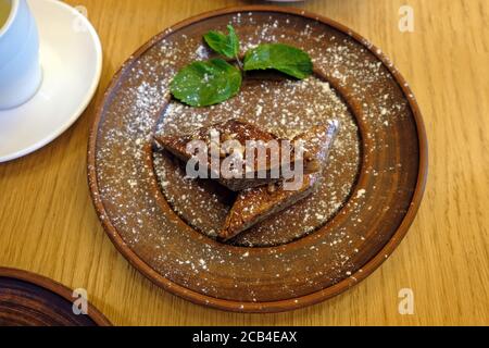 Baklava con noci su una piastra di argilla vista dall'alto. Due pezzi di baklava cosparsi di polvere e decorati con una foglia di menta. Dolci turchi con noci Foto Stock