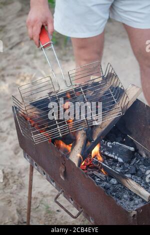 Legna da ardere con fiamma attraverso griglie barbecue sulla spiaggia, estate pic-nic concetto Foto Stock