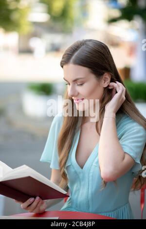 Affascinante femmina dai capelli castani, libro di lettura, stropicciando i capelli Foto Stock