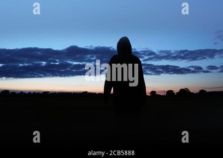 Una misteriosa figura agganciata, di nuovo alla fotocamera. Silhouette, guardando il tramonto. Foto Stock