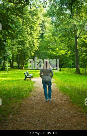 donna bionda in piedi in un parco circondato da alberi e silenzio, comunione con la natura e l'anima ricerca concetto Foto Stock