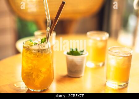 Limonata chiara di bevanda gialla di benessere, kombucha di ghiaccio di frutta, tè di semi di chia verde con cannuccia di vetro riutilizzabile in vetro su tavolo di legno. Sole abbagliamento foto Foto Stock