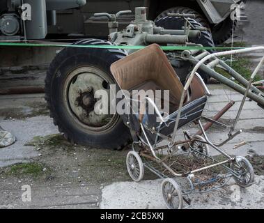 PRAM vintage arrugginita con agenti atmosferici e veicolo militare in cortile Foto Stock