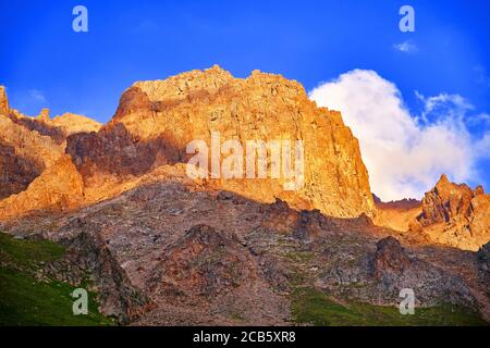 Enormi scogliere sullo sfondo del cielo blu con nuvole alla luce del sole che tramonta; maestosa vista delle montagne al tramonto Foto Stock