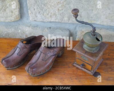 vecchio macinacaffè a mano antico e zoccoli di pelle su vecchio scrivania in legno con sfondo a parete in sandsotone Foto Stock