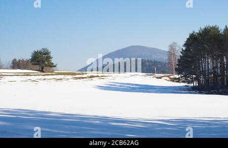 campo invernale e campagna forestale paesaggio innevato con alberi, collina e alto sedile in legno nella montagna luzicke hory Foto Stock