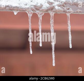 primo piano icicles appesi giù dal tetto di stagno, fuoco selettivo, sfondo arancione inverno congelato Foto Stock