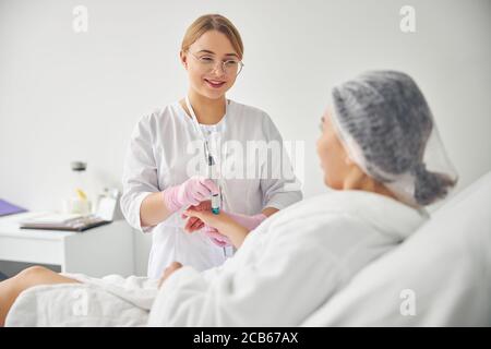 Giovane dermatologo amichevole che conduce una procedura cosmetica Foto Stock