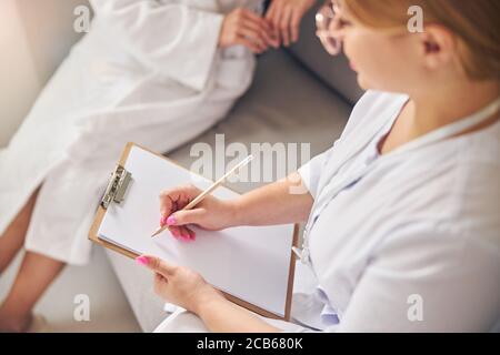 Cosmetician prende appunti sulla sua cliente femminile Foto Stock