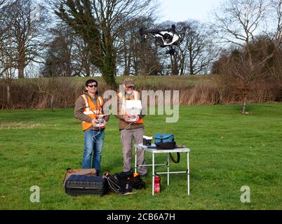 Due fotografi si divertono a volare un drone con una fotocamera inserita Un ampio giardino di campagna nel Cotswolds Foto Stock