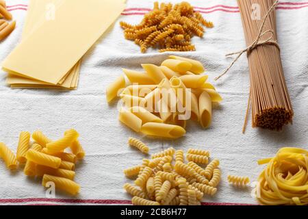 Uncookes tipi di pasta italiana su tovagliolo di lino bianco, primi piani di cibo Foto Stock