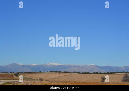 La Sierra de Madrid con neve in cima e un campo asciutto, in Spagna. Foto Stock