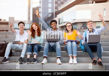Studenti multirazziali che alzano le mani in aria e agitando Foto Stock