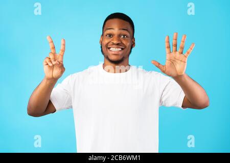 Black Man che mostra il numero sette sorridendo alla fotocamera, sfondo blu Foto Stock