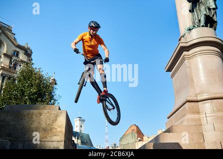 Vista da sotto l'uomo estremo che tiene in mano una bici sportiva e che pende in aria. Ciclista guardando giù quando fa trucco. Concetto di trucco. Foto Stock