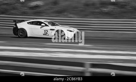 Una panoramica monocromatica di un'auto da corsa mentre si circuito una pista. Foto Stock