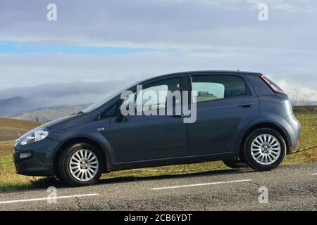 Pienza, Italia - 13 ottobre 2012: Fiat punto Evo auto parcheggiata di fronte al meraviglioso paesaggio con colline con autumns campi di grano e vecchio castello visto t Foto Stock