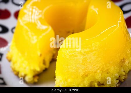 Pezzo di Quindim, piccolo budino tagliato da uovo brasiliano, con zucchero e cocco grattugiato. Foto macro o closeup della cucina brasiliana Foto Stock