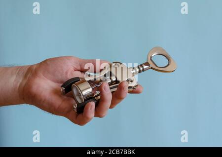 L'uomo adulto tiene in mano un cavatappi di metallo. Stappatura di bottiglie di vino. Maschio di razza europea, 43-45 anni. Utensili da cucina Foto Stock