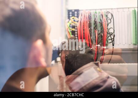 Il tecnico dell'elettricista verifica gli impianti elettrici e i fili sul sistema di protezione relè. Unità di controllo vano. Gruppo di comando a media tensione Foto Stock