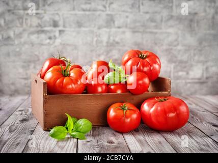 Scatola di legno piena di pomodori maturi, rossi e succosi raccolti Foto Stock