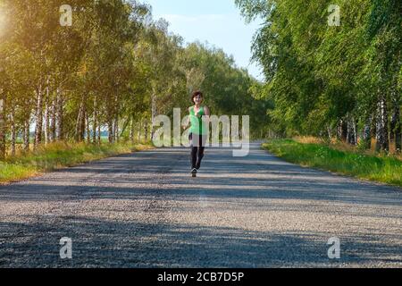 giovane donna bianca di fitness corre giù il centro di una strada di campagna, vista frontale. Foto Stock