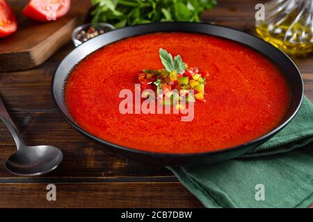 Primo piano di un piatto con la rinfrescante zuppa di tomatoe estiva gazpacho su sfondo rustico scuro Foto Stock