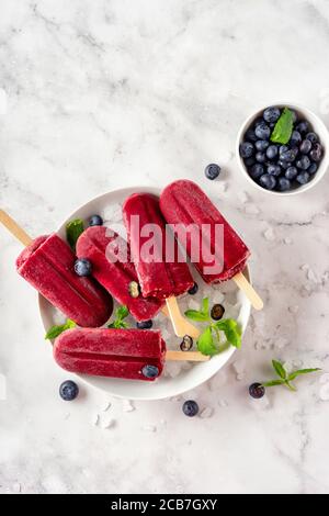 Pop-sicel di sorbetto al mirtillo vegano colorati e rinfrescanti in un bianco piastra Foto Stock