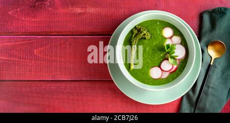 Vista dall'alto di una zuppa verde di spinaci broccolini sfondo rosso rustico Foto Stock