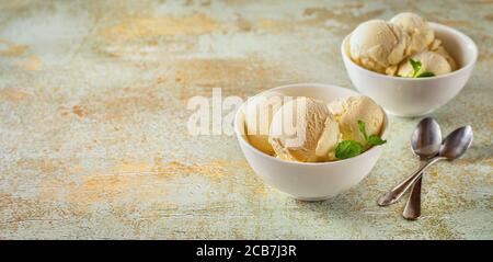 Scoop di gelato alla vaniglia in ciotole bianche su sfondo pastello Foto Stock