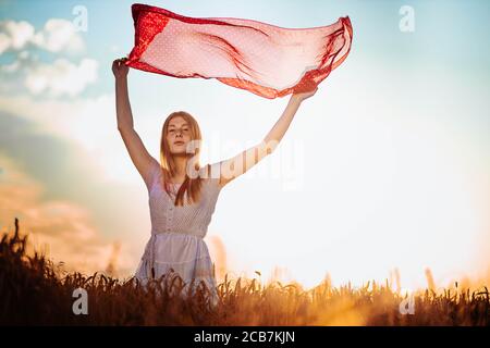 All'aperto foto di giovane, zenzero ragazza in abito bianco che tiene una sciarpa rossa che si accende in aria. Spazio di copia Foto Stock