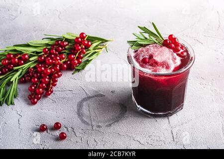 Cocktail di frutta fresca ghiacciata in vetro, rinfrescante bevanda estiva al ribes rosso con foglia di rosmarino su fondo di pietra in cemento, vista angolare Foto Stock