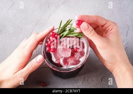 Le mani della donna contengono bacche di ribes per la preparazione di cocktail di frutta fresca ghiacciata in vetro con foglia di rosmarino, fondo di pietra in cemento Foto Stock