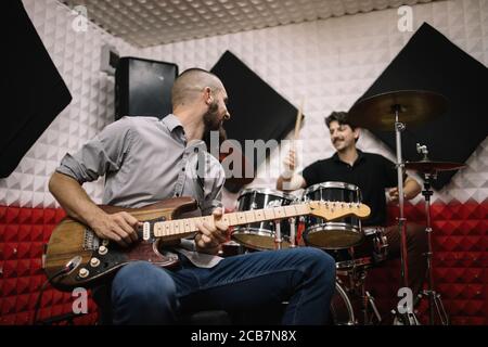 Chitarrista e batterista che suonano strumenti musicali. I membri della rock band suonano chitarra e drum set presso lo studio musicale. Foto Stock