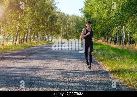 giovane donna bianca forma fisica corre lungo paese lato strada, vista frontale. Foto Stock