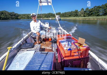 Diemitz, Germania. 06 agosto 2020. Jens Winkelmann è in movimento con il suo chiosco d'acqua sul Vilzsee di fronte alla serratura di Diemitz e fornisce ai vacanzieri su case galleggianti, yacht e canoe ghiaccio, bevande fredde o pesce appena affumicato. (Girato con un lungo periodo di esposizione) ogni giorno in stagione si trova sui corsi d'acqua e sul lago al confine con lo stato del Brandeburgo e del Meclemburgo per un massimo di 80 chilometri. Il Brandeburgo ha convertito la sua vecchia chiatta lunga quattro metri in una sorta di "consumo galleggiante" con un congelatore e scatole di conservazione del fresco. Credit: Jens Büttner/dpa-Zentr/dpa/Alamy Live News Foto Stock