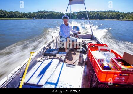 Diemitz, Germania. 06 agosto 2020. Jens Winkelmann è in movimento con il suo chiosco d'acqua sul Vilzsee di fronte alla serratura di Diemitz e fornisce ai vacanzieri su case galleggianti, yacht e canoe ghiaccio, bevande fredde o pesce appena affumicato. (Girato con un lungo periodo di esposizione) ogni giorno in stagione si trova sui corsi d'acqua e sul lago al confine con lo stato del Brandeburgo e del Meclemburgo per un massimo di 80 chilometri. Il Brandeburgo ha convertito la sua vecchia chiatta lunga quattro metri in una sorta di "consumo galleggiante" con un congelatore e scatole di conservazione del fresco. Credit: Jens Büttner/dpa-Zentr/dpa/Alamy Live News Foto Stock