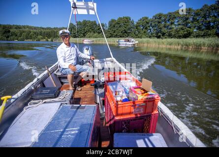 Diemitz, Germania. 06 agosto 2020. Jens Winkelmann è in movimento con il suo chiosco d'acqua sul Vilzsee di fronte alla serratura di Diemitz e fornisce ai vacanzieri su case galleggianti, yacht e canoe ghiaccio, bevande fredde o pesce appena affumicato. (Girato con un lungo periodo di esposizione) ogni giorno in stagione si trova sui corsi d'acqua e sul lago al confine con lo stato del Brandeburgo e del Meclemburgo per un massimo di 80 chilometri. Il Brandeburgo ha convertito la sua vecchia chiatta lunga quattro metri in una sorta di "consumo galleggiante" con un congelatore e scatole di conservazione del fresco. Credit: Jens Büttner/dpa-Zentr/dpa/Alamy Live News Foto Stock