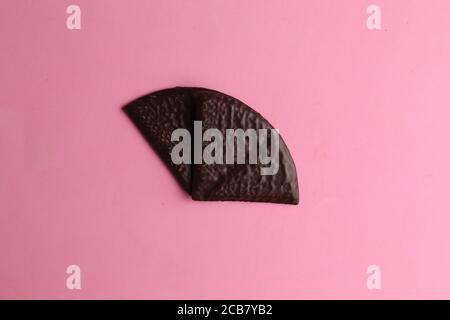 Primo piano di un biscotto coperto di cioccolato isolato su una superficie rosa Foto Stock