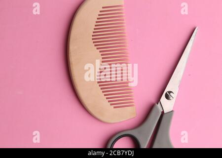 Vista dall'alto delle forbici e di un pettine di legno su a. sfondo rosa Foto Stock