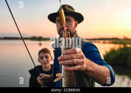 Uomo positivo con il ragazzo adolescente in piedi insieme e che mostra cattura del pesce all'aperto Foto Stock
