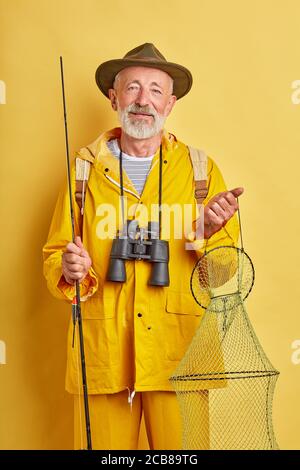 Vecchio pescatore bearded con rete binoculare di tenuta, Rod. Sport.close up di ricreazione foto. Sfondo giallo isolato, scatto studio. Stile di vita Foto Stock