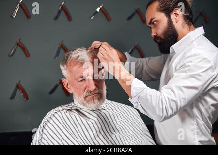 Anziano pensionato attivo che ottiene il taglio dei capelli dal barbiere esperto dentro barber's shop.close up photo Foto Stock