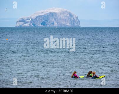 Tre ragazze in mare con body board e Bass Rock gannet colonia all'orizzonte, Firth of Forth, East Lothian, Scozia, Regno Unito Foto Stock