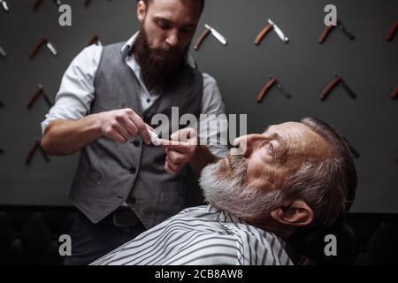 Caucasin uomo vecchio ottenendo la sua barba rasata dal barbiere hairtician in visita al salone di rasatura, close up Foto Stock