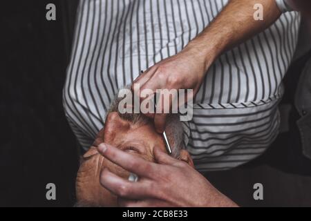 Senior rispettabile uomo caucasico visitando un parrucchiere in un barbiere per la rasatura e la creazione di un nuovo design per il suo grigio dai capelli barba Foto Stock