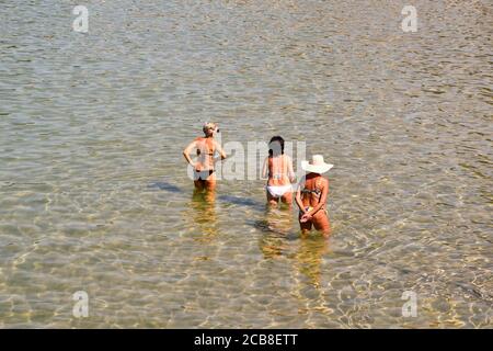 Vista ad alto angolo di tre donne da dietro rinfrescandosi nelle acque della riva in estate, Liguria, Italia Foto Stock
